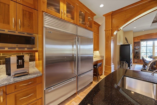 kitchen with sink, built in appliances, tasteful backsplash, light stone countertops, and light wood-type flooring