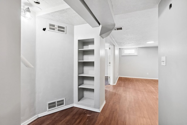 corridor featuring wood-type flooring, a textured ceiling, and built in shelves