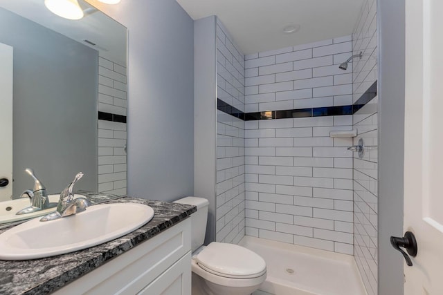 bathroom with a tile shower, vanity, and toilet