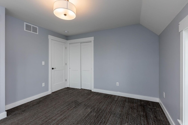 unfurnished bedroom with dark colored carpet, vaulted ceiling, and a closet