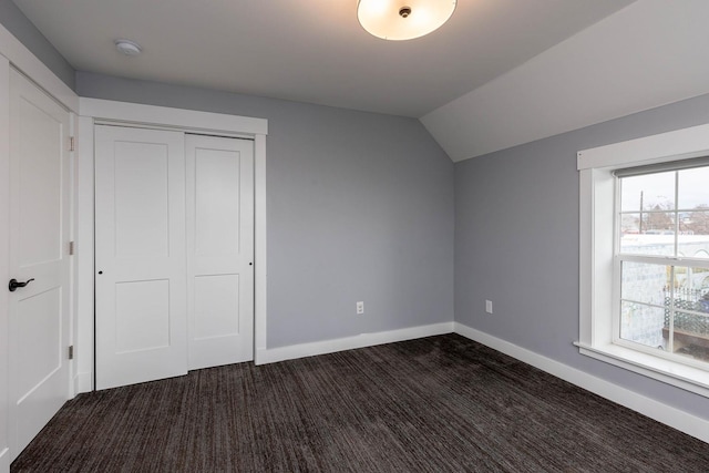 unfurnished bedroom with lofted ceiling, a closet, and dark colored carpet