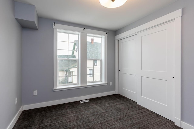 unfurnished bedroom with dark carpet and a closet