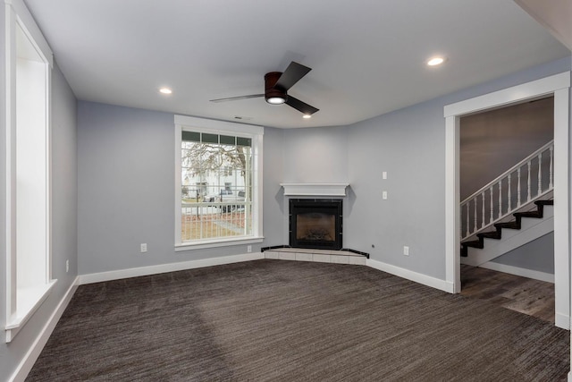 unfurnished living room with dark carpet, a fireplace, and ceiling fan