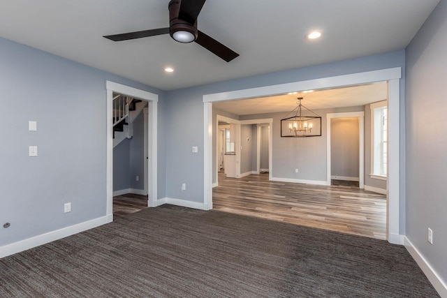 unfurnished room featuring ceiling fan with notable chandelier and dark carpet