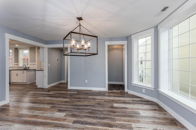 unfurnished dining area featuring sink, a notable chandelier, and dark hardwood / wood-style floors