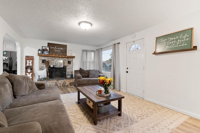 living room featuring a stone fireplace, light hardwood / wood-style floors, and a textured ceiling