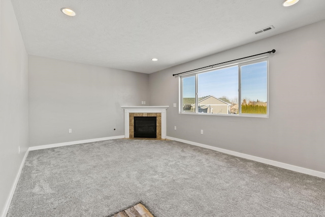 unfurnished living room featuring a tiled fireplace, carpet floors, and a textured ceiling