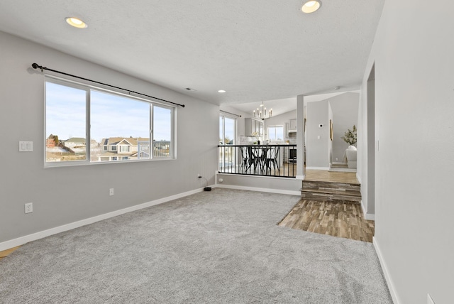 spare room with a textured ceiling, vaulted ceiling, a chandelier, and carpet