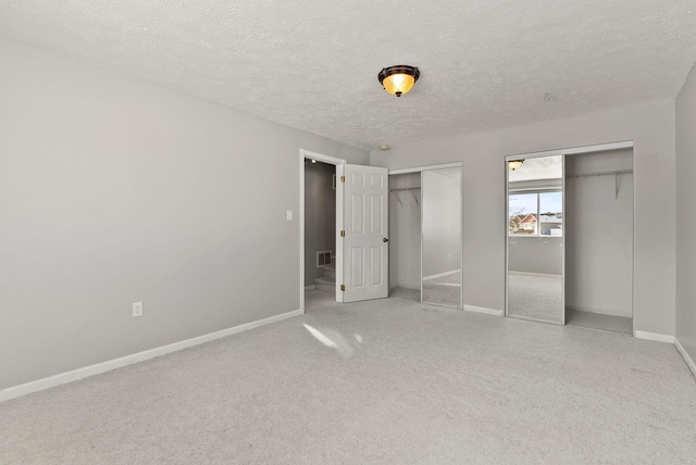 unfurnished bedroom with multiple closets, carpet flooring, and a textured ceiling