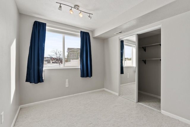 unfurnished bedroom with multiple windows, light colored carpet, a textured ceiling, and a closet