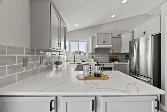 kitchen with stainless steel refrigerator with ice dispenser, vaulted ceiling, light stone counters, and gray cabinetry