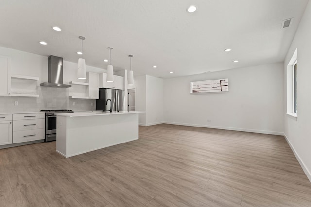 kitchen featuring pendant lighting, white cabinets, stainless steel appliances, a center island with sink, and wall chimney range hood