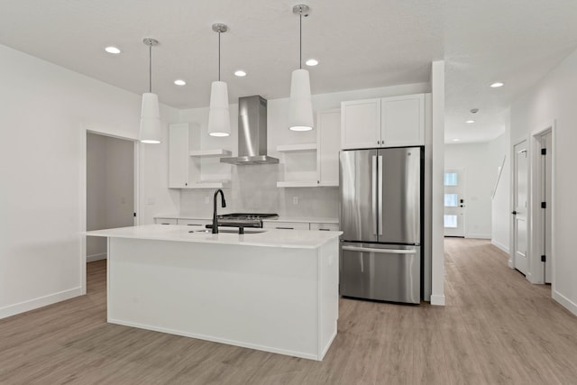 kitchen featuring pendant lighting, wall chimney range hood, sink, stainless steel refrigerator, and white cabinets