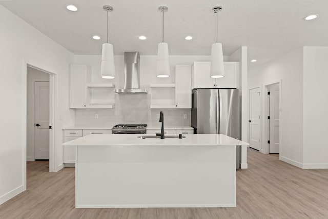 kitchen with sink, stainless steel fridge, wall chimney range hood, a kitchen island with sink, and white cabinets