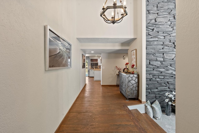 corridor with a notable chandelier, a towering ceiling, and dark hardwood / wood-style floors