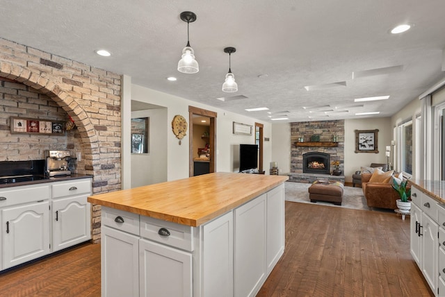 kitchen featuring a fireplace, decorative light fixtures, white cabinetry, butcher block counters, and a textured ceiling