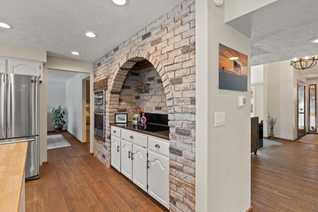 kitchen with a textured ceiling, dark wood-type flooring, white cabinets, and appliances with stainless steel finishes