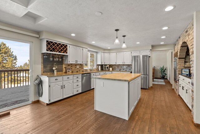 kitchen with wood-type flooring, a center island, hanging light fixtures, stainless steel appliances, and white cabinets