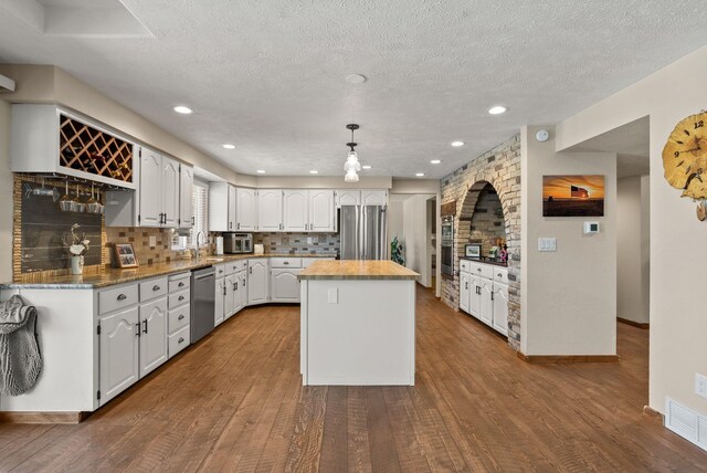 kitchen with appliances with stainless steel finishes, hanging light fixtures, a kitchen island, and white cabinets