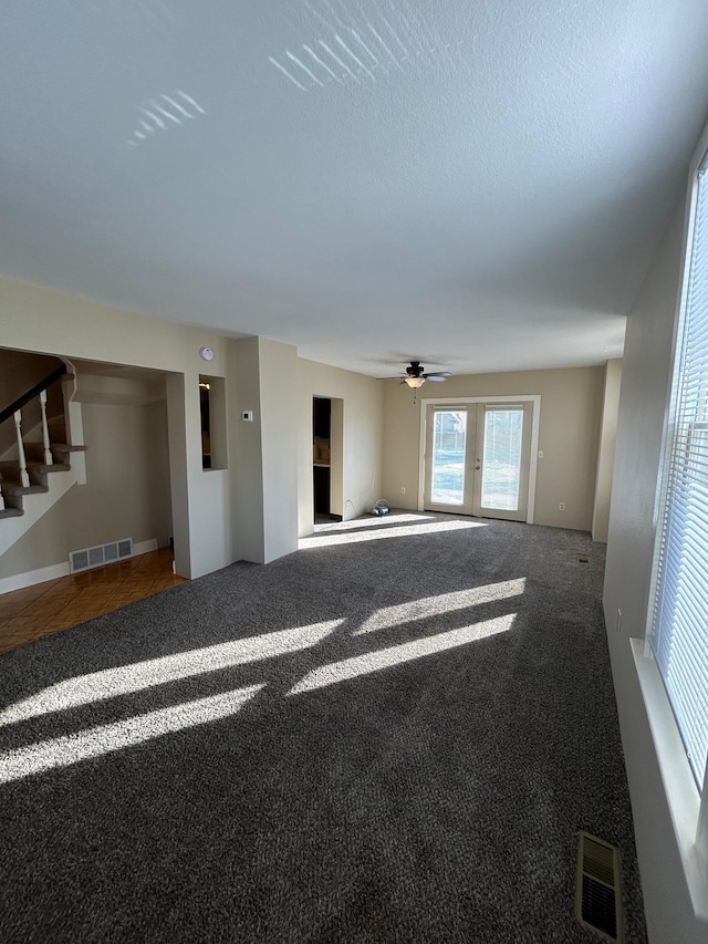 unfurnished living room featuring carpet, stairs, a ceiling fan, and visible vents