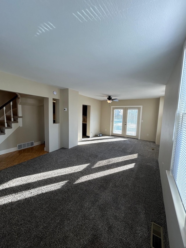 unfurnished living room featuring visible vents, carpet flooring, stairway, and a ceiling fan