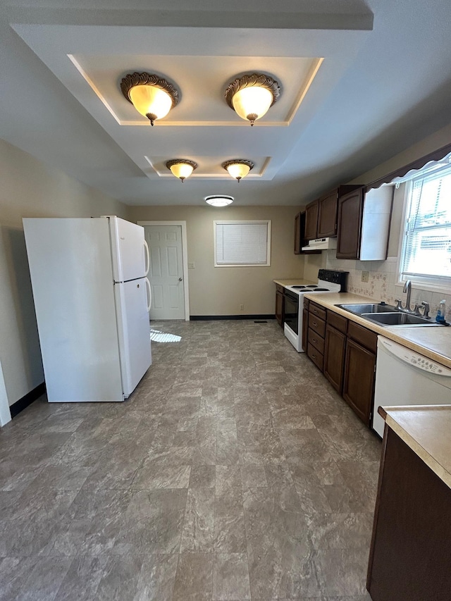 kitchen with dark brown cabinetry, light countertops, white appliances, a raised ceiling, and a sink