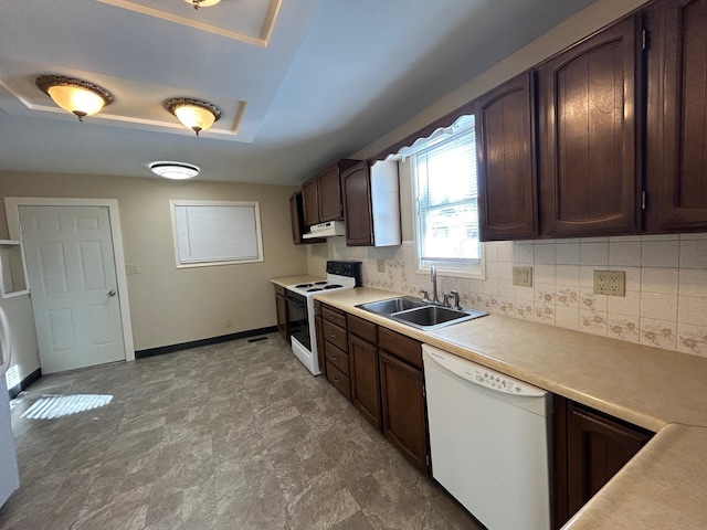 kitchen featuring under cabinet range hood, light countertops, decorative backsplash, white appliances, and a sink