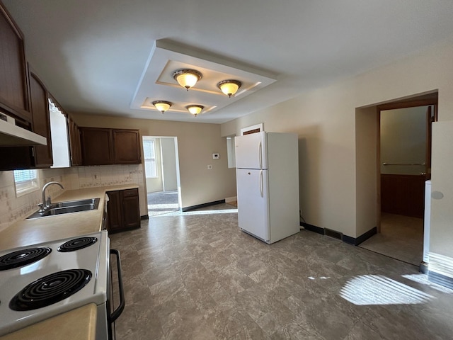 kitchen featuring a raised ceiling, a sink, white appliances, baseboards, and dark brown cabinets