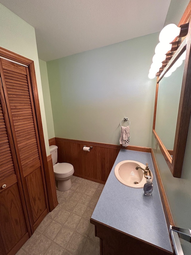 bathroom featuring tile patterned floors, toilet, wooden walls, wainscoting, and vanity