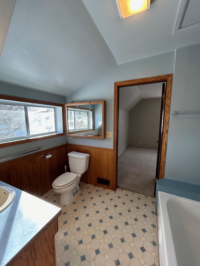 full bath with tile patterned floors, a wainscoted wall, toilet, wood walls, and vaulted ceiling