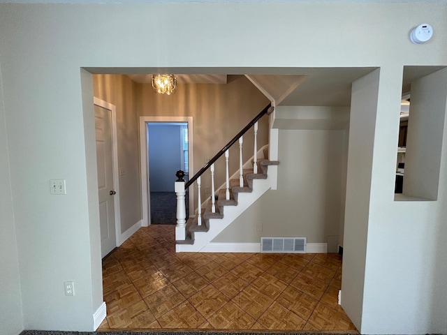 stairway featuring a notable chandelier, visible vents, and baseboards