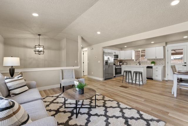 living room featuring sink, an inviting chandelier, vaulted ceiling, a textured ceiling, and light wood-type flooring