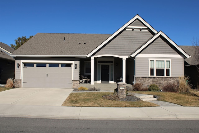 craftsman-style house with roof with shingles, covered porch, concrete driveway, an attached garage, and stone siding