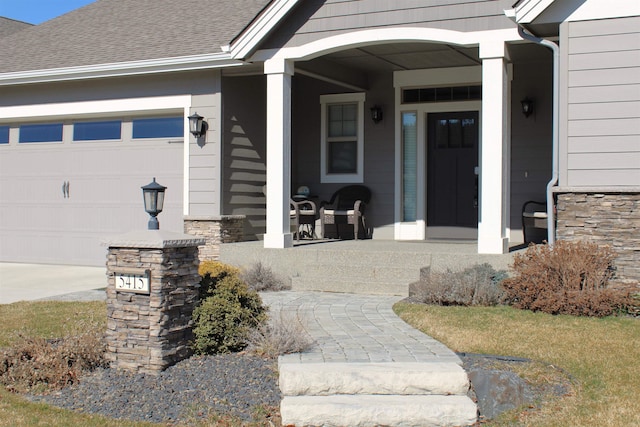 view of exterior entry with stone siding, covered porch, a shingled roof, and an attached garage