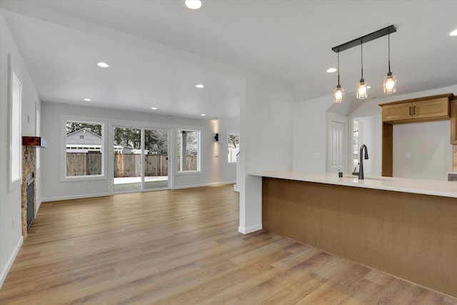 kitchen with pendant lighting, a stone fireplace, sink, and light hardwood / wood-style flooring