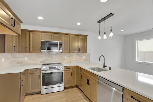 kitchen featuring appliances with stainless steel finishes, pendant lighting, sink, light hardwood / wood-style floors, and kitchen peninsula