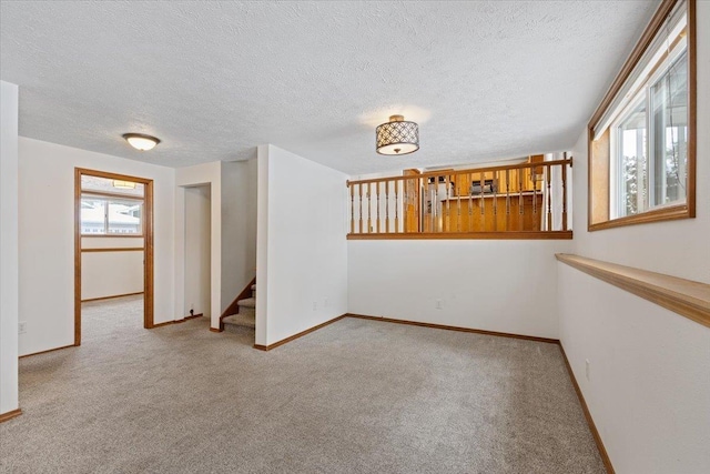 carpeted empty room with stairway, baseboards, and a textured ceiling