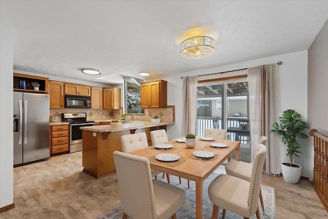 kitchen with brown cabinets, light countertops, a peninsula, tasteful backsplash, and appliances with stainless steel finishes