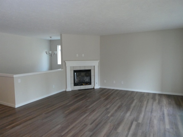 unfurnished living room with dark wood-type flooring, an inviting chandelier, and a tile fireplace