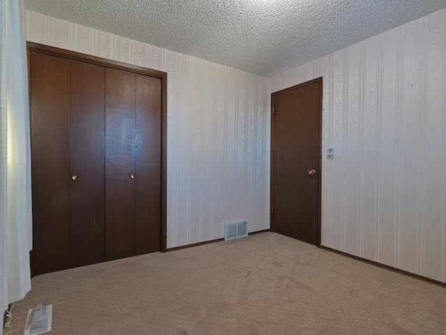 unfurnished bedroom with light carpet, a closet, and a textured ceiling