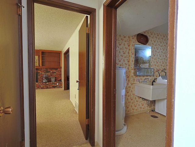 corridor featuring sink, light colored carpet, electric water heater, and a textured ceiling