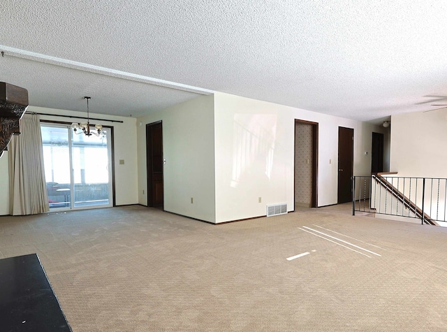 carpeted spare room featuring an inviting chandelier and a textured ceiling