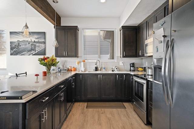 kitchen featuring appliances with stainless steel finishes, sink, decorative backsplash, hanging light fixtures, and light hardwood / wood-style floors