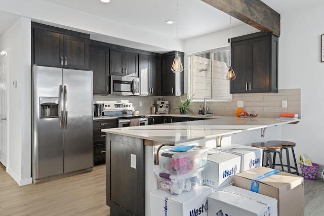 kitchen with sink, a breakfast bar area, decorative light fixtures, light wood-type flooring, and stainless steel appliances