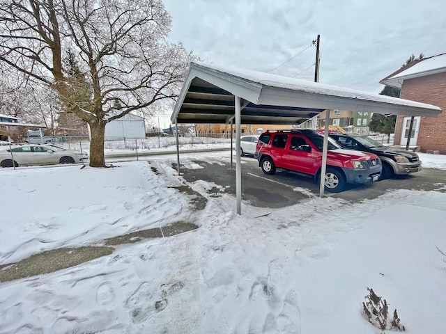 snow covered parking area featuring a carport