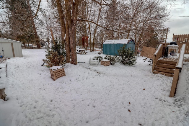 yard covered in snow with a wooden deck and a storage unit