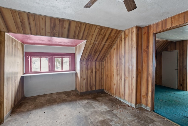 additional living space with lofted ceiling, a textured ceiling, wooden walls, and ceiling fan