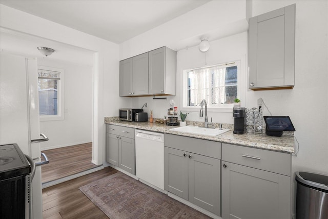 kitchen with appliances with stainless steel finishes, sink, gray cabinetry, dark hardwood / wood-style flooring, and light stone counters