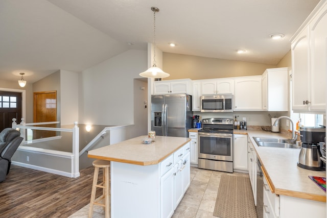 kitchen with sink, a kitchen island, decorative light fixtures, stainless steel appliances, and white cabinets