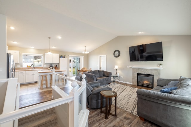 living room with light hardwood / wood-style floors, lofted ceiling, a tiled fireplace, and sink